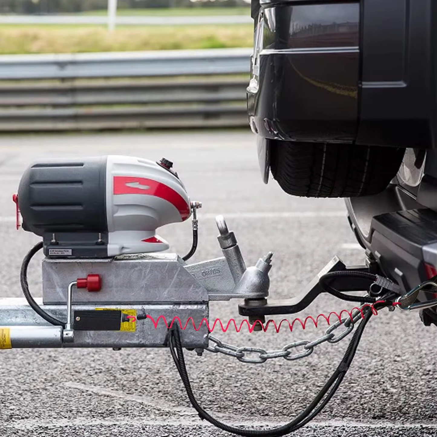 Red coiled breakaway lanyard running from a caravan A-frame breakaway switch to a weight distribution hitch on a red ute, with safety chains crossed underneath